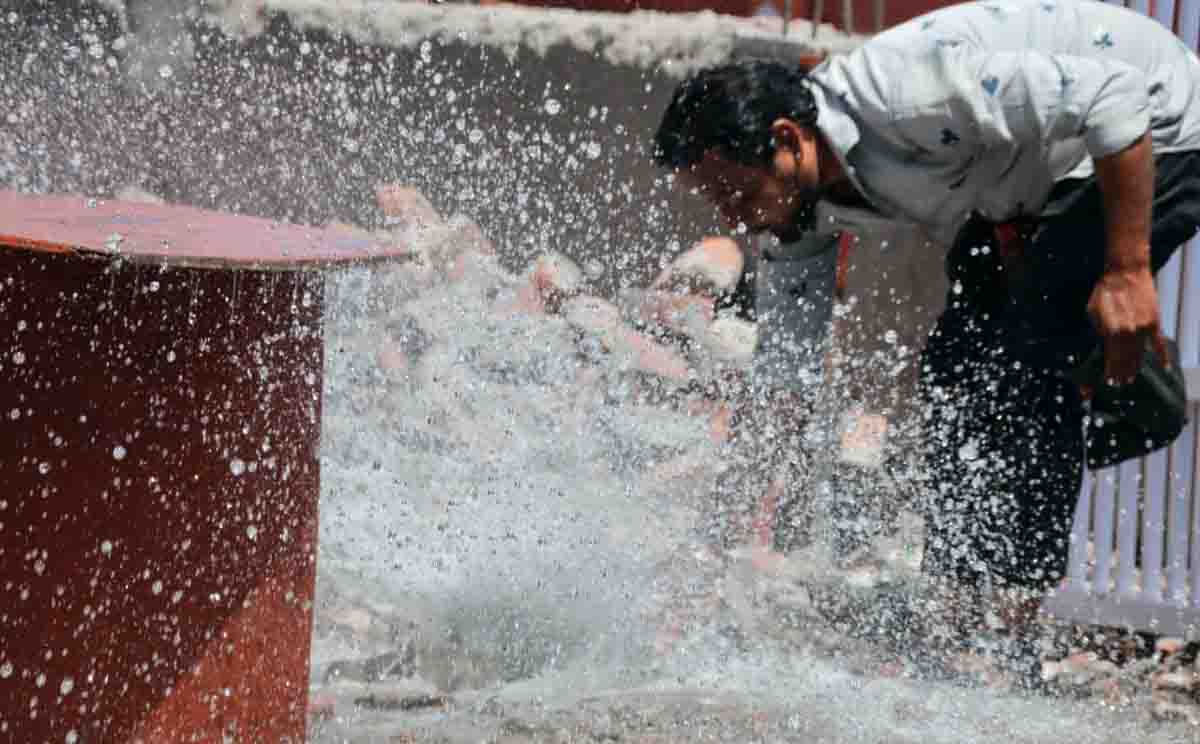 A man seeks relief from the heat by drinking water and splashing his face at a leaking water pipe on a hot day in Dehradun